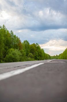 Country road with markings in the middle of the forest. Path and forward movement in the sun. Beautiful, green forest in the spring at sunset. Concept for success in the future goal and passing time