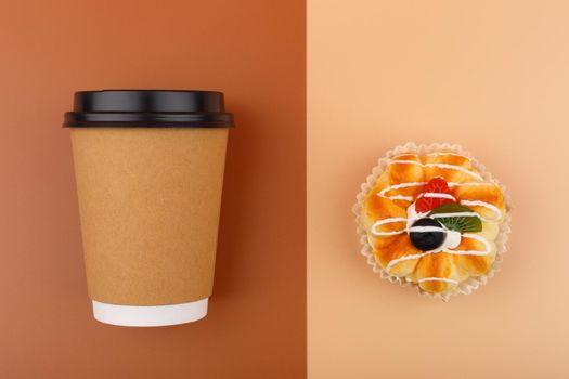 Top view of coffee or tea in brown cardboard cup with pastry against brown and beige background. Concept of hot drinks, take away food, small breaks or cheat meal