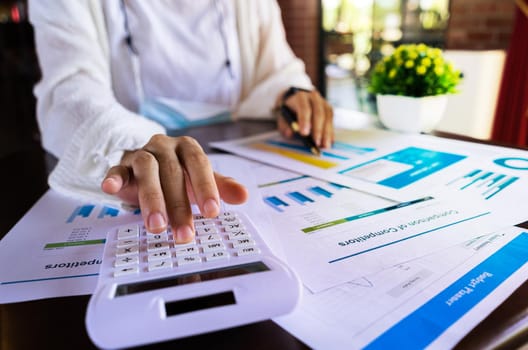 Close up businesswoman hand using a calculator and pointing graph report document about cost, tax, profit, income at the office.