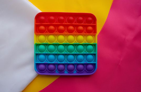 The rainbow toy lies against a background of pink and yellow white fabric. Blue and Orange Funny Interactive Anti-Stress Silicone Toys. Pop it.