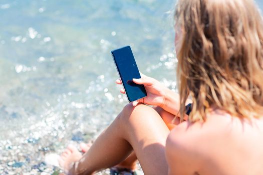 Teenage girl playing games and searching web on the telephone on the beach. Gadget dependency disorder problem for kids during holiday vacation at the seaside concept