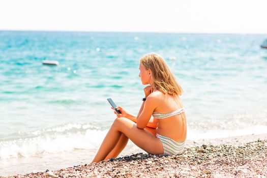 Teenage girl playing games and searching web on the telephone on the beach. Gadget dependency disorder problem for kids during holiday vacation at the seaside concept