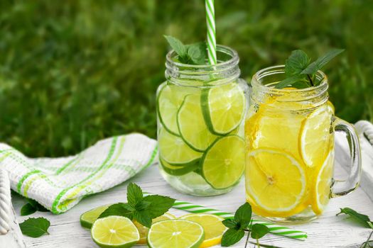 Cold refreshing homemade lemonade with mint, lemon and lime in mason jars on a summer lawn, copyspace.