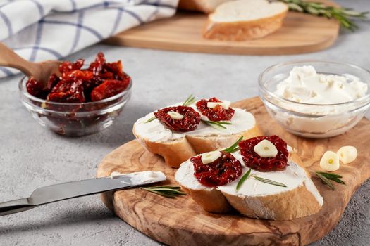 Homemade sandwiches with cream cheese and sun-dried tomatoes on a wooden board of olive - delicious healthy breakfast, italian cuisine.