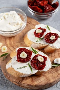 Homemade sandwiches with cream cheese and sun-dried tomatoes on a wooden board of olive - delicious healthy breakfast, italian cuisine, vertical image, copy space.