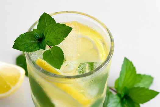 Fresh homemade cocktail with lemon, mint and ice on a white table, close up.