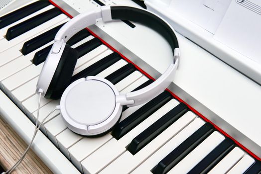 white headphones lie on the keyboard of the electronic piano.