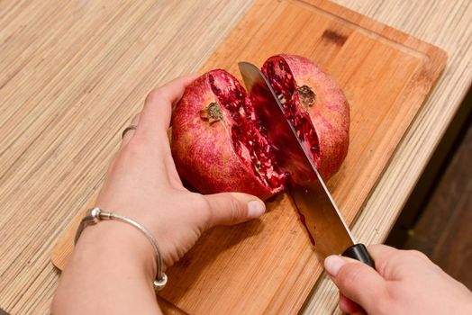 Female hands Cutting pomegranate on a wood cut board in a kitchen. Close-up.