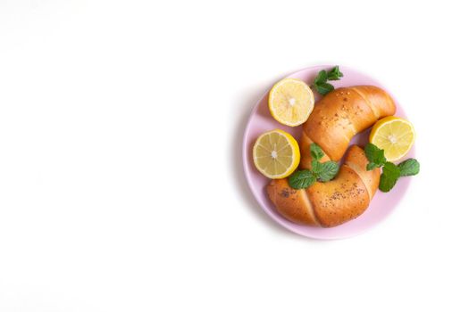 Close-up top view on a white surface two pastry bagels lie on a pink ceramic plate with lemon halves and mint leaves. Selective focus. Copy space.