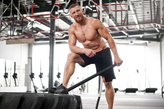 Man gym hammer hit tractor wheel hitting huge tire Athlete sportive man Middle adult handsome sportsman bodybuilder weightlifter ideal body indoor naked torso Exercise endurance cross training