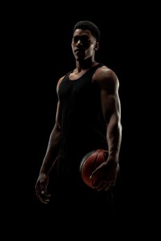 Basketball player holding a ball against black background. Serious concentrated african american man.