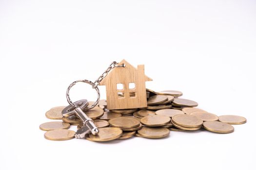 House keys with house shaped keychain on stack money coins, isolated on white background.