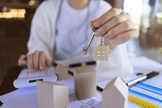 Professional Real estate agents showing house keys and calculate the price of house to customers with the model houses, house design documents.