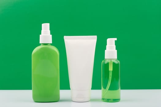 Set of green and white cosmetic bottles against yellow background. Concept of organic beauty products with natural ingredients. Moisturizing body spray, face cream and cleansing gel for face.