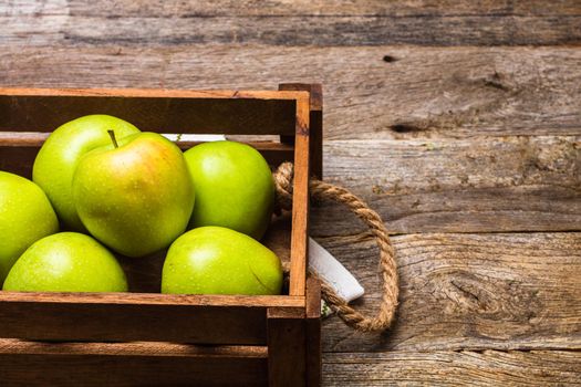 Wooden crate with ripe green apples on wooden table.