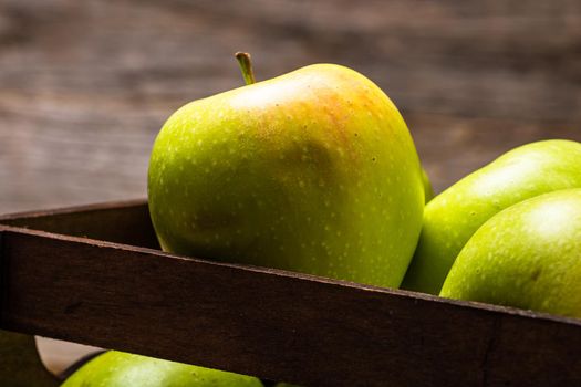 Wooden crate with ripe green apples on wooden table.