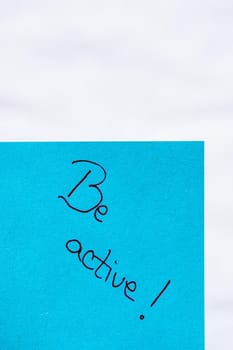 Be active handwriting text close up isolated on blue paper with copy space. Writing text on memo post reminder