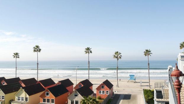 Colorful waterfront cottages, Oceanside California USA. Multicolor bungalow huts, summer sea, beachfront lodging. Many vacation houses on beach, ocean waves and palm trees. Lifeguard tower, watchtower