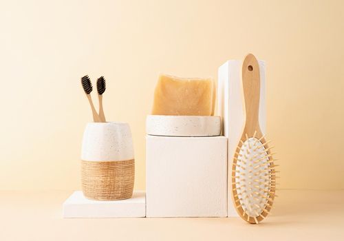 Natural organic selfcare products. Handmade soap, wooden brush and bamboo toothbrushes on white podiums. Spa accessories creative art composition on beige background