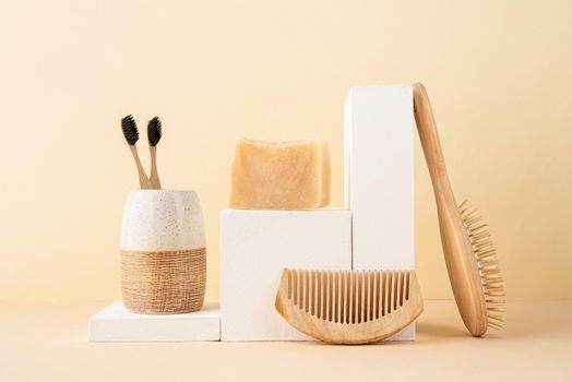 Natural organic selfcare products. Handmade soap, wooden brush and bamboo toothbrushes on white podiums. Spa accessories creative art composition on beige background