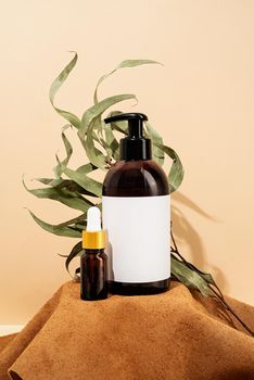 Natural organic selfcare products. Brown bottles mockup for natural cosmetics, spa accessories on brown leather podium, cream background and leaves. Spa accessories creative art composition on beige background