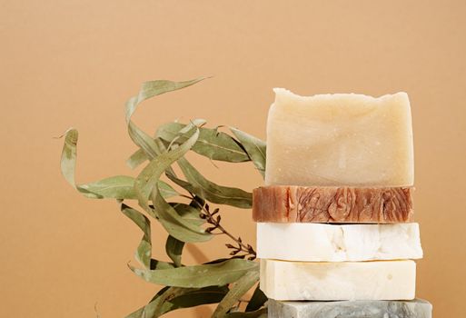 Natural organic selfcare products. Tower stack of different handmade soaps and leaves on cream background. Spa accessories creative art composition on beige background