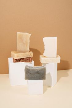 Natural organic selfcare products. Different handmade soaps composition on white podiums on cream background. Spa accessories creative art composition on beige background
