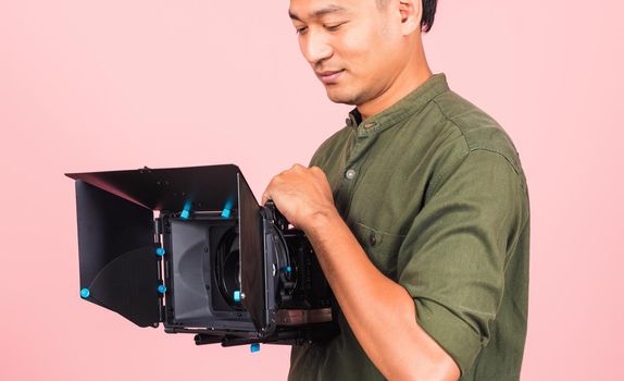 Portrait of Asian handsome young adult man confident professional videographer handheld holding digital video camera with matte box for cinema, studio shot isolated on pink background