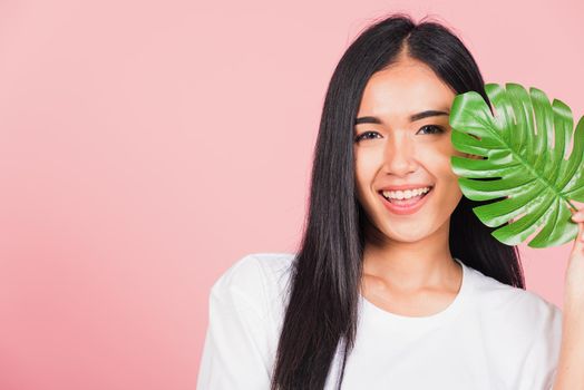 Beauty face. Portrait of Asian beautiful young woman with fresh healthy skin hold green monstera leaf on her face, Tropical Leaves, studio shot isolated on pink background, Skin body care spa concept