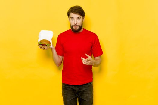 Hamburgers in a box and an emotional man in a red T-shirt on a yellow background