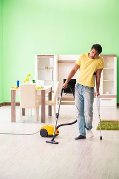 Injured man on crutches vacuum cleaning house