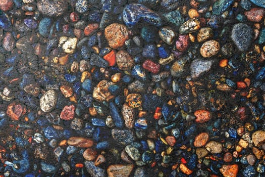 Dark texture of asphalt mixed with many small multi-colored stones