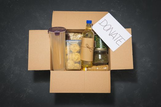 Donation box with various food. Open cardboard box with oil, canned food, cereals and pasta.