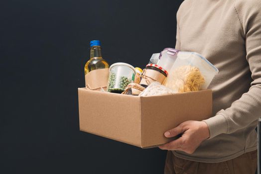 donation help box full of supplies. Volunteer in protective medical hand gloves holding food box for delivery charity 