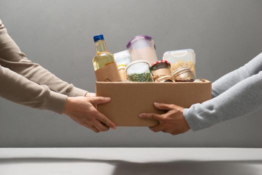 Volunteers with donation box with foodstuffs on grey background