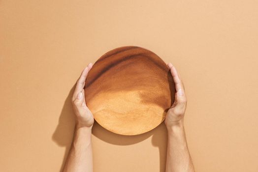Male two hands hold empty dish on beige background
