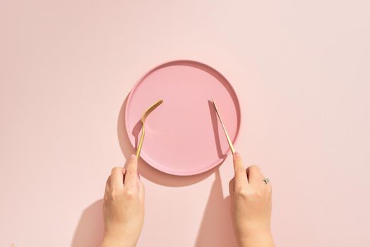 Hands hold a fork and knife over plate on pink background