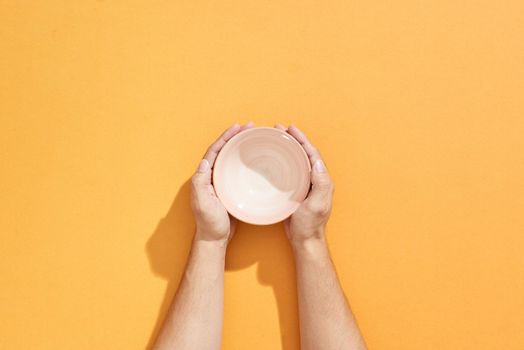 Man holds an empty bowl in his hands over orange