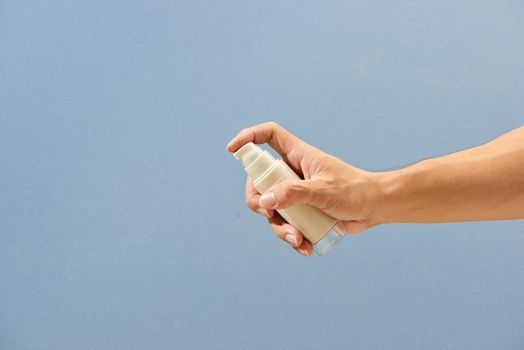 Hand holding spray bottle isolated on light blue background with clipping path.