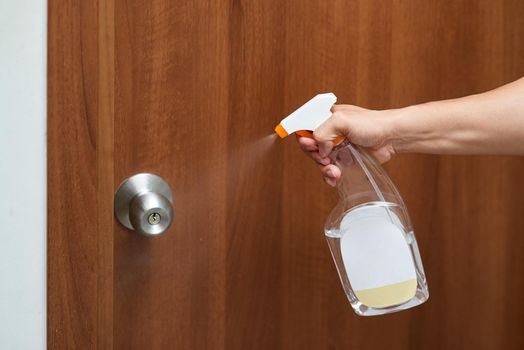Hand hold bottle alcohol spraying disinfecting door.