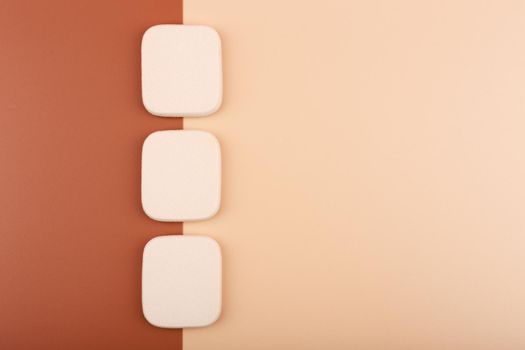 Top view of three square shaped make up sponges on beige and brown backgrounds. Concept of make up and matching foundation for different skin tones