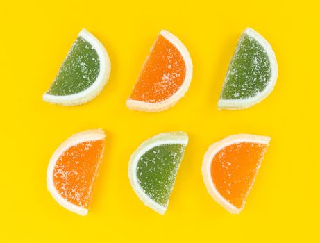 Orange and green marmalade citrus slices in sugar on a yellow background.