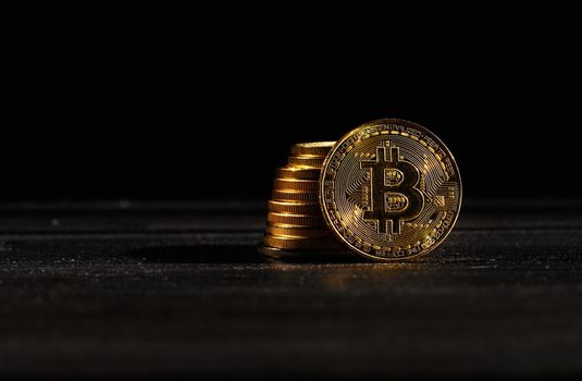 Leader in cryptocurrency bitcoin BTC on a top of coins against black wooden surface. Closeup golden coin with bitcoin logo. Stack of decentralized digital currency. Crypto payment. Electronic money