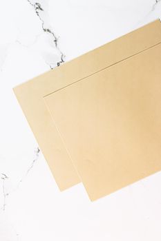 Beige A4 papers on white marble background as office stationery flatlay, luxury branding flat lay and brand identity design for mockups