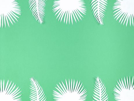 Tropical paper leaves on a green background, flat lay with copy space.