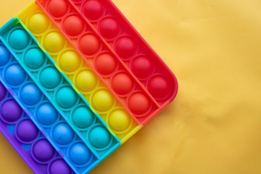 A rainbow toy lies against a background of yellow fabric. Blue and Orange Funny Interactive Anti-Stress Silicone Toys. Pop it.
