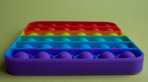 A rainbow toy lies on a yellow background. Blue and Orange Funny Interactive Anti-Stress Silicone Toys. Pop it.