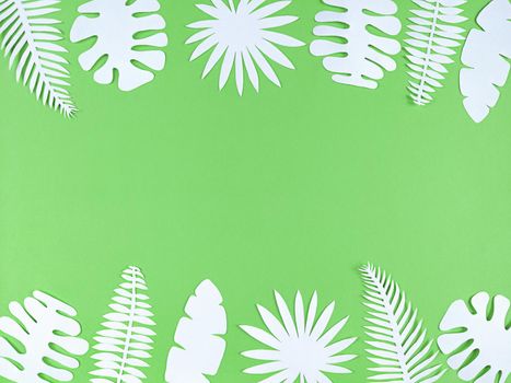 Tropical paper leaves on a green background, flat lay with copy space.