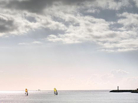 Windsurfer men on a windsurfs.  Gentle wind blowing, afternoon sun glittering in sea waves