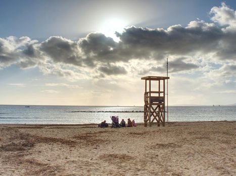 Women with children resting and playing on the beach at life guard wooden watch. Lazy Sunday afternoon at coastline. Palma de Malorca 26th of January 2020.